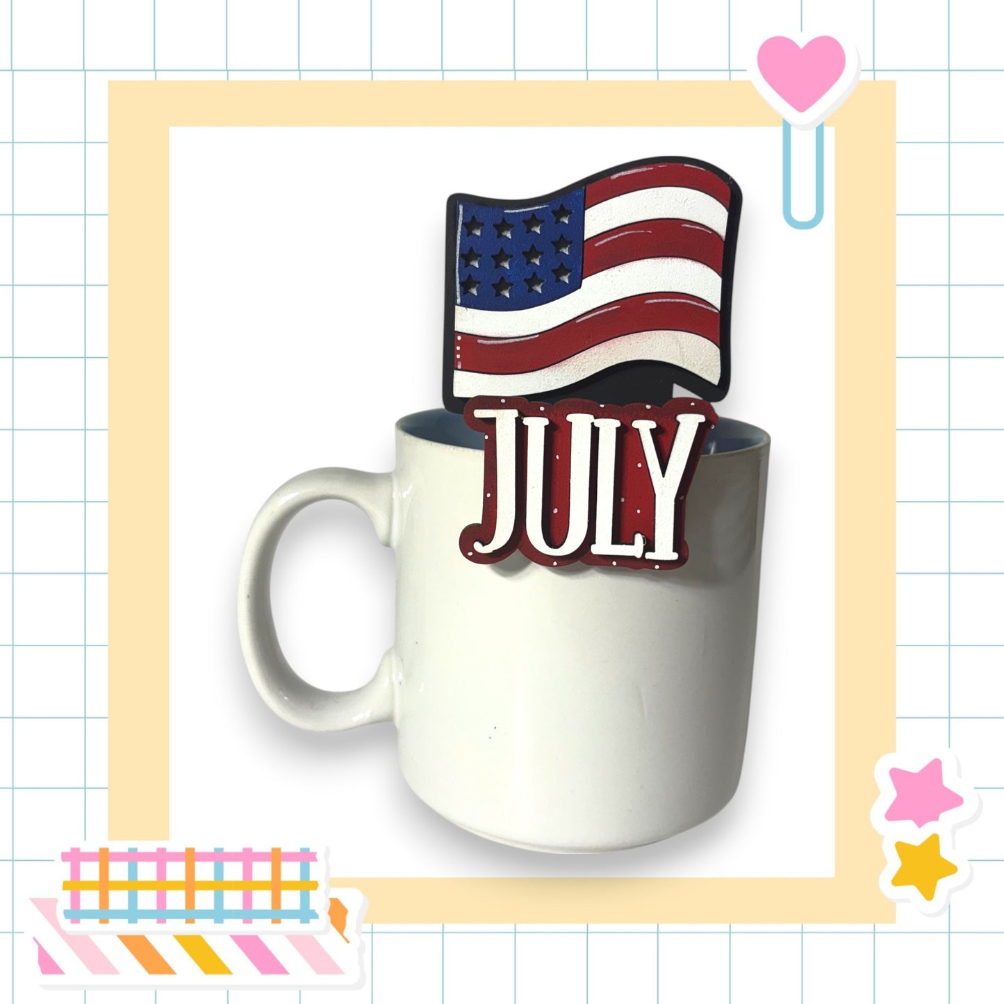 A white mug with a patriotic American flag sticker on top, and the word "JULY" written on it, set against a background with a grid pattern.