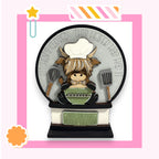 A decorative snow globe with a cartoon cow wearing a chef's hat and holding a spoon and a bowl, surrounded by kitchen utensils.