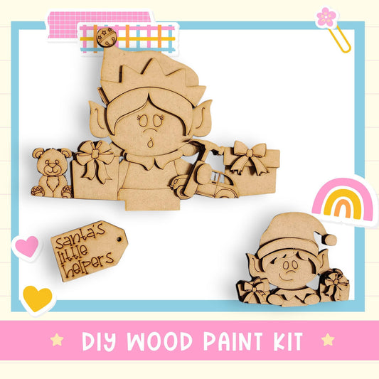 The image is a DIY wood paint kit featuring a wooden elf and a wooden teddy bear, along with a tag that says "Santa's little helpers".