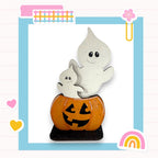 A Halloween-themed image featuring a carved pumpkin with a ghost figure sitting inside it, set against a blue background with various colorful and whimsical elements.