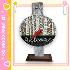 a wooden sign with a red cardinal bird perched on it, surrounded by a snowy forest scene. The sign is hanging on a wooden post, and the word "Welcome" is written on it.