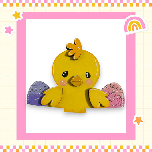 A cheerful yellow cartoon chicken with colorful Easter eggs on its wings is depicted in a pink and yellow checkered frame.
