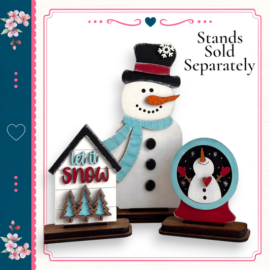 A snowman and a snow globe are displayed on a stand, with the text "Let it snow" and "stands sold separately" written above them.