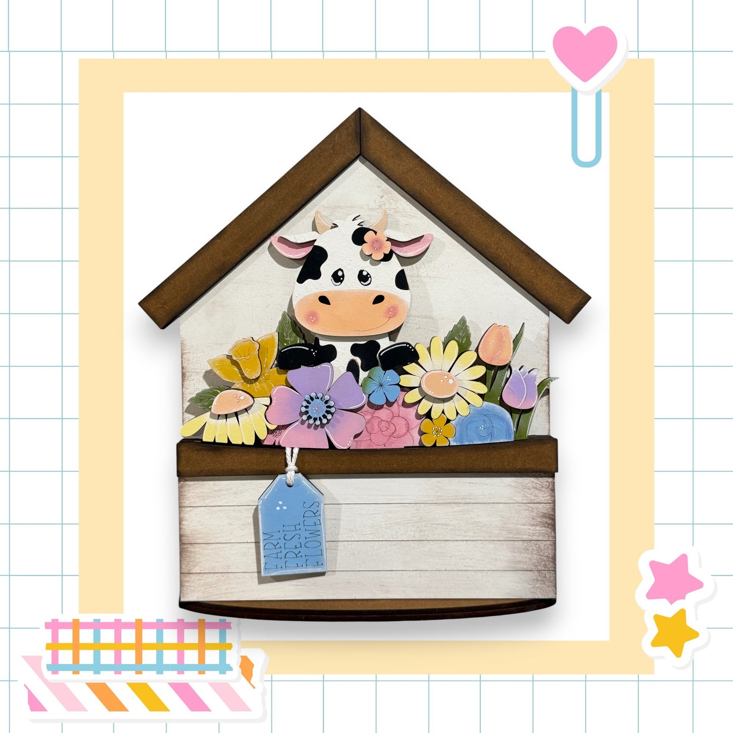 A wooden house-shaped structure with a cow decoration on it, surrounded by a variety of colorful flowers.