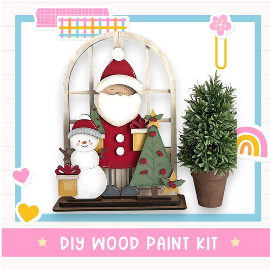A DIY wood paint kit featuring a wooden frame with a Santa Claus and a snowman figure, along with a potted plant and a rainbow-colored sticker.