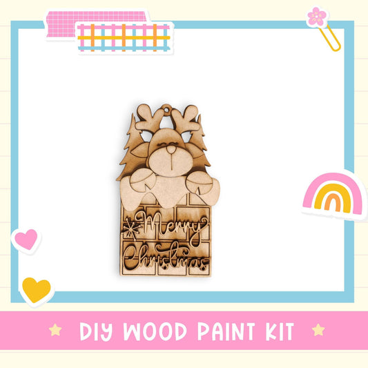 A DIY wood paint kit with a wooden ornament featuring a reindeer and Christmas trees, along with a "Merry Christmas" message.