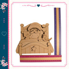 A wooden Santa Claus figure sitting on a bed, with a bird perched on his shoulder. The Santa figure is made of wood and appears to be carved. The bed is made of wood and has a star on it. The image also includes a ruler and a heart, suggesting it may be a decorative or artistic piece.