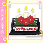 A black wooden bench with a sign that says "Joy to the World" in front of it, decorated with red poinsettia flowers and lit candles.