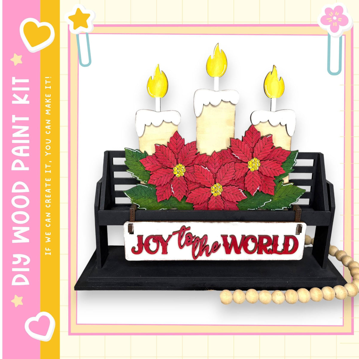 A black wooden bench with a sign that says "Joy to the World" in front of it, decorated with red poinsettia flowers and lit candles.