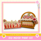 a DIY wood paint kit for creating a wooden sign with the words "Barn Fresh Berries" and a wooden basket with strawberries. The kit appears to be made of wood and includes the necessary materials for creating a wooden sign and a wooden basket.