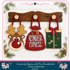 A festive arrangement of three wooden ornaments, including a reindeer, a gift bag, and a star, displayed on a wooden shelf against a white background with greenery and holiday decorations.