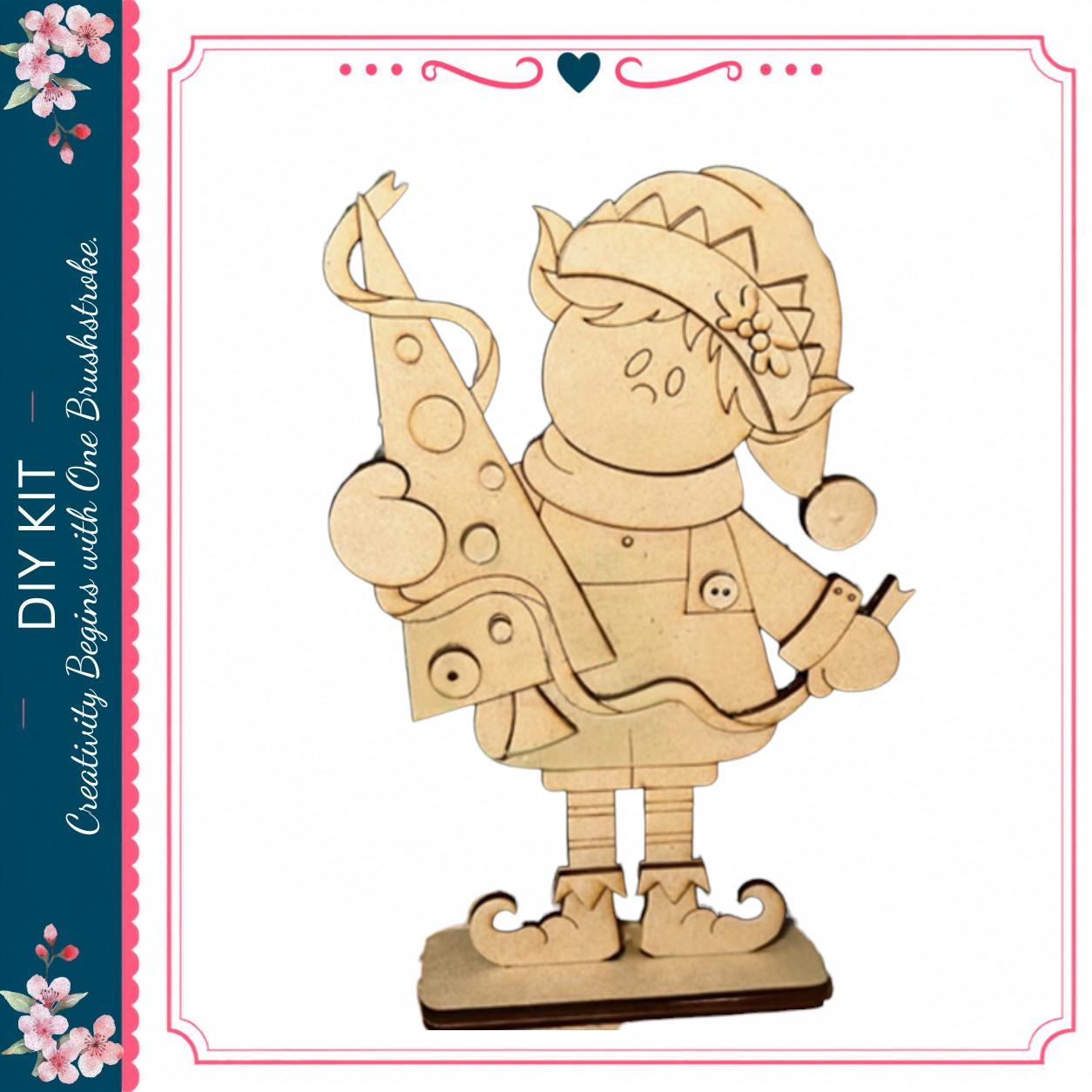 A wooden figure of an elf holding a piece of paper, likely a drawing or painting of a Christmas tree.