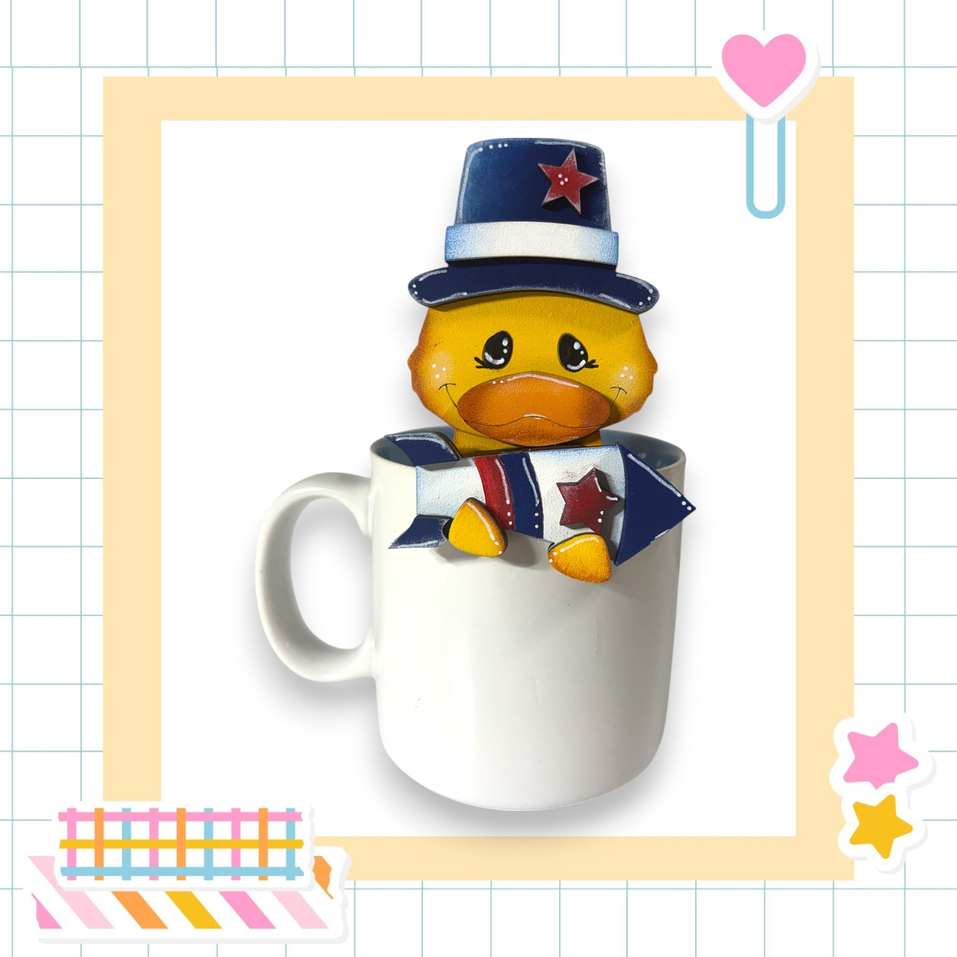 A yellow duck wearing a blue hat with a red star sits inside a white mug, surrounded by colorful stickers and a heart-shaped object.