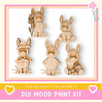 a DIY wood paint kit with five wooden animal figurines, including a donkey, a rabbit, and a bird, each holding a flower. The kit appears to be designed for children to create their own wooden animal characters.