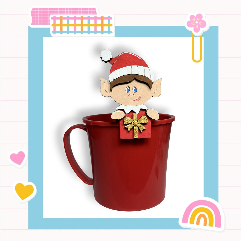 A red mug with a cartoon elf figure holding a gift box on top, set against a colorful background with various decorative elements.