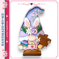 A hand-made Easter decoration featuring a whimsical gnome figure with a purple hat adorned with flowers and a sign that reads "Happy Easter".
