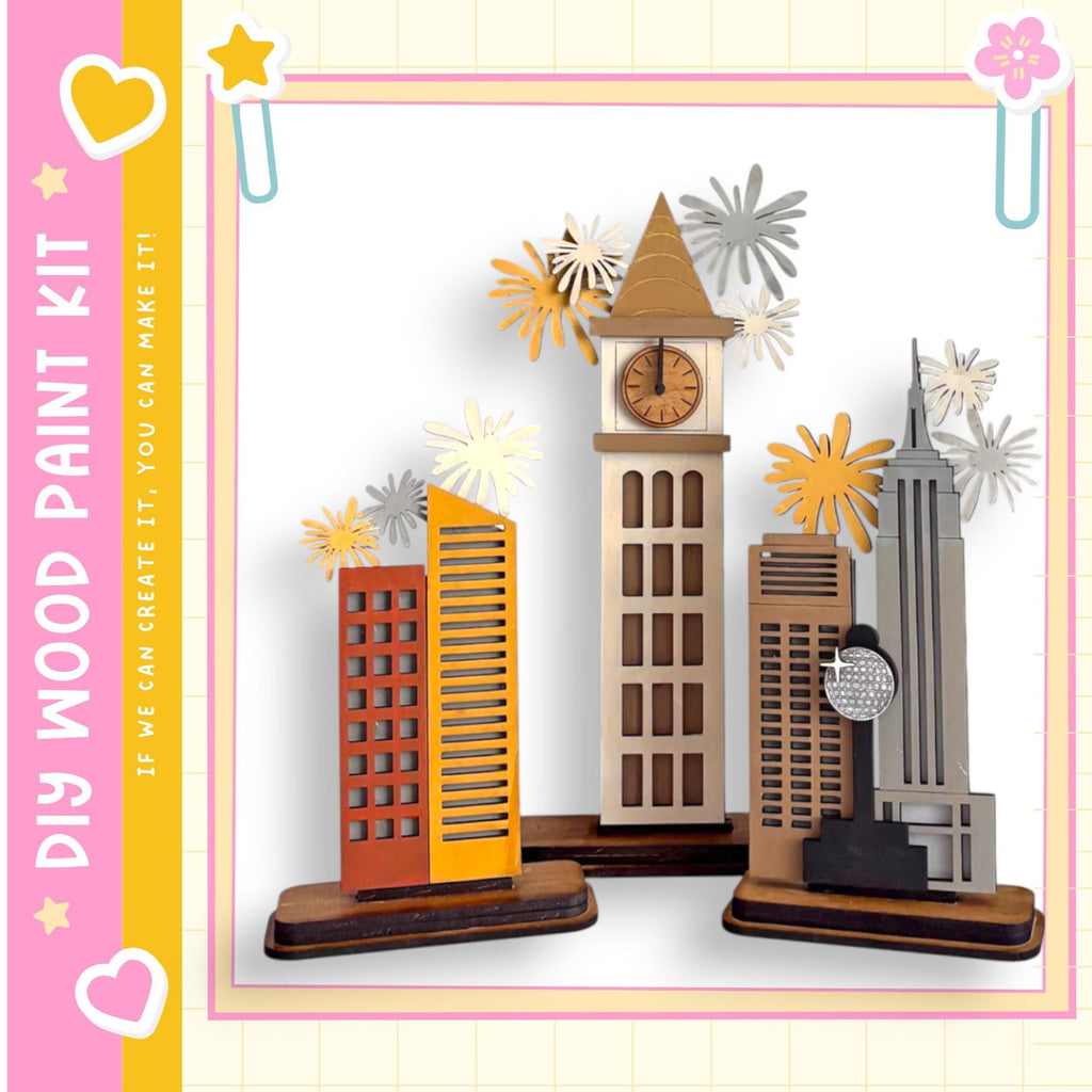 A wooden paint kit featuring a miniature cityscape with various buildings, including a clock tower, surrounded by decorative paper flowers.