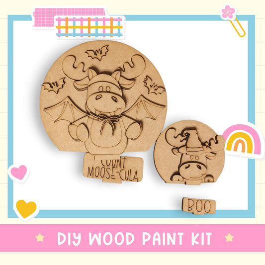 a DIY wood paint kit for creating wooden shapes, including a moose and a bat. The kit includes a moose and a bat, along with a "Count Moose-Cula" label. The kit is presented in a colorful and playful manner, with a background that includes a rainbow and a heart.