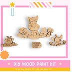 The image is a colorful advertisement for a DIY wood paint kit, featuring a cartoon Santa Claus and other festive decorations.