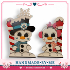 two snowmen, one wearing a black top hat and the other wearing a pink bow, sitting on a red and white striped pole.
