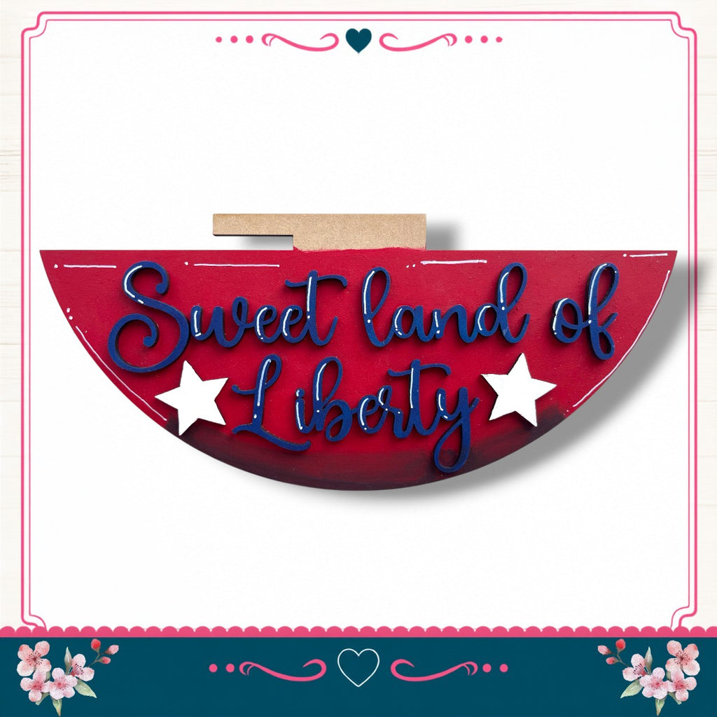 a red sign with the text "Sweet land of Liberty" written on it, surrounded by a decorative border with pink and blue floral elements.