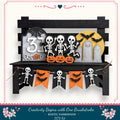 A Halloween-themed display featuring skeleton decorations, pumpkins, and a gravestone, all set against a black wooden background.