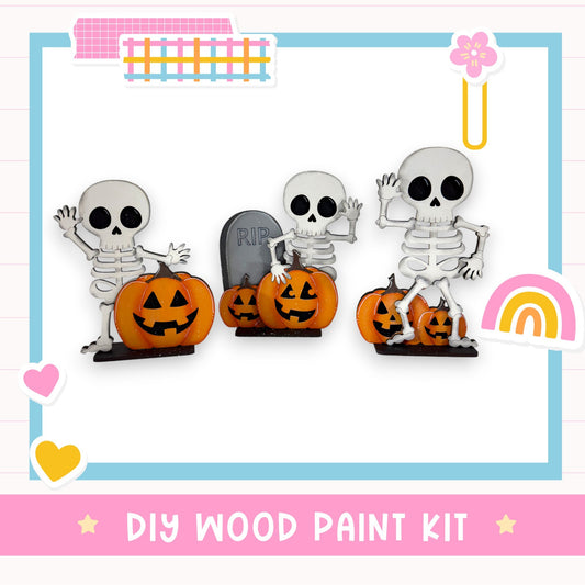 A DIY wood paint kit featuring three skeleton figurines holding carved pumpkins, with a pink and blue border and various decorative elements.
