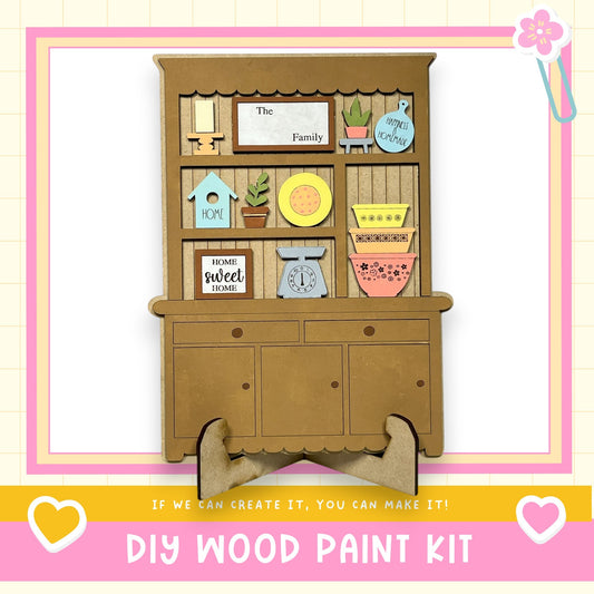 The image is a DIY wood paint kit advertisement, featuring a wooden hutch with various decorative elements such as a birdhouse, a clock, and a bowl. The text on the image encourages viewers to "If we can create it, you can make it!" and provides a "DIY WOOD PAINT KIT" for creating custom wooden pieces.