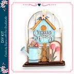 a wooden birdhouse with a sign that says "Hello Spring" and a watering can with flowers.