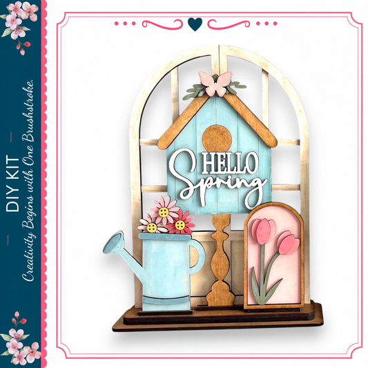 a wooden birdhouse with a sign that says "Hello Spring" and a watering can with flowers.