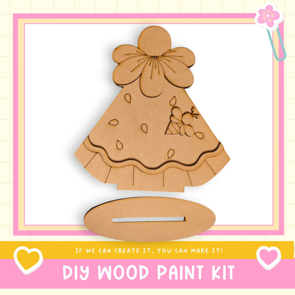 a DIY wood paint kit, including a wooden dress and a wooden stand, with a pink and white border.
