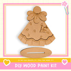 a DIY wood paint kit, including a wooden dress and a wooden stand, with a pink and white border.