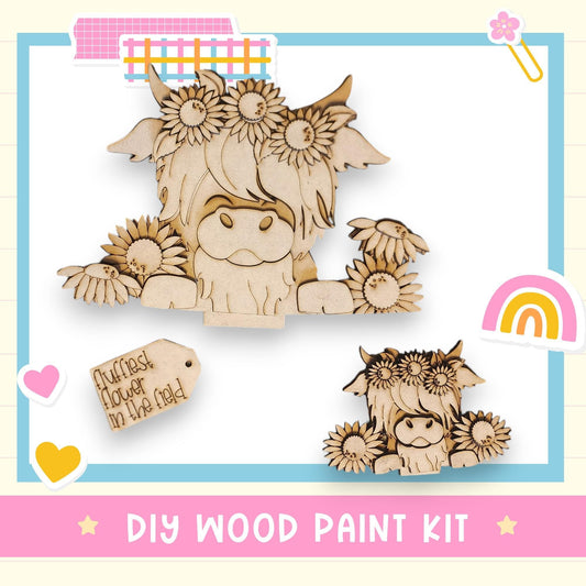 The image is a DIY wood paint kit featuring two wooden cow figurines with flower crowns, surrounded by various decorative elements such as hearts, a rainbow, and a tag.