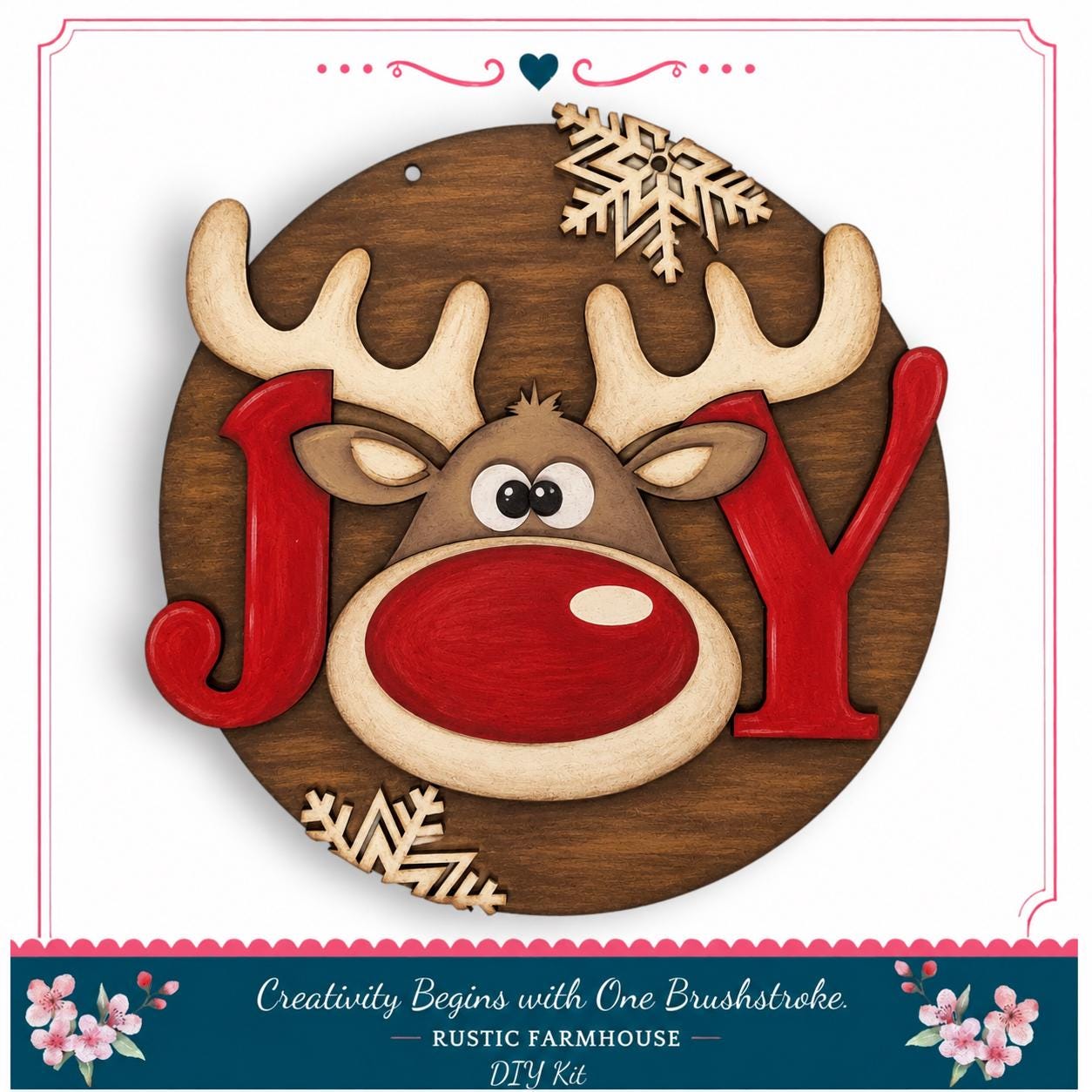 A wooden sign featuring a reindeer's face with the word "Joy" written in red letters, surrounded by snowflakes and flowers.