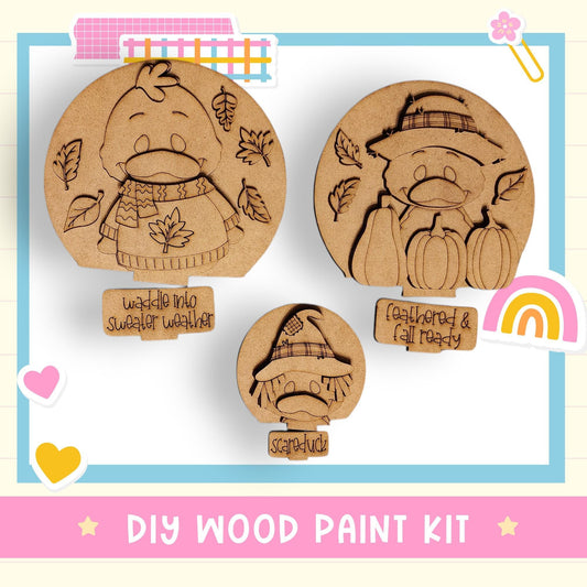The image is a DIY wood paint kit featuring three wooden shapes, including a bird, a cat, and a squirrel, each with a unique design. The shapes are set against a background with a rainbow and a heart.
