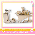 The image is a DIY wood paint kit featuring a wooden boot and a wooden wheelbarrow filled with flowers.