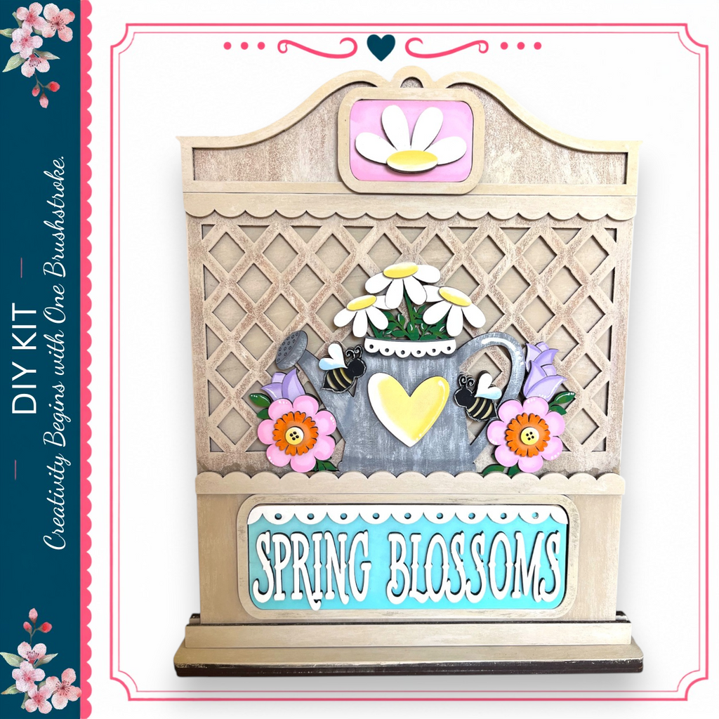 The image is a wooden sign with a decorative design, featuring a teapot, flowers, and a heart. The sign has the text "Spring Blossoms" written on it.