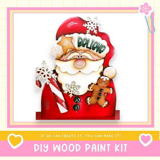 A festive DIY wood paint kit featuring a decorated Santa Claus figure with a gingerbread man and snowflakes, along with the text "If we can create it, you can make it!"