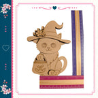 A wooden cutout of a cat wearing a witch's hat and holding a carved pumpkin, with a ruler placed next to it.