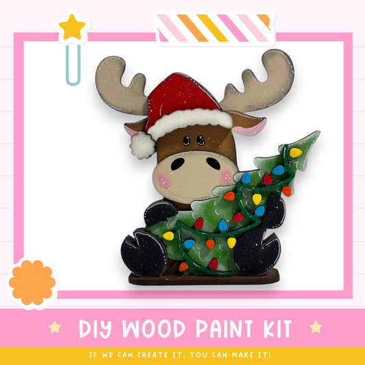 A wooden toy moose wearing a Santa hat and holding a decorated Christmas tree.