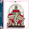 A DIY kit featuring a gingerbread man and a girl, with the word "JOY" displayed on a green sign.