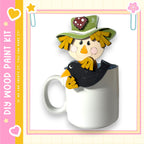 A wooden paint kit featuring a scarecrow figure sitting inside a white mug, with a heart and star design on the mug.