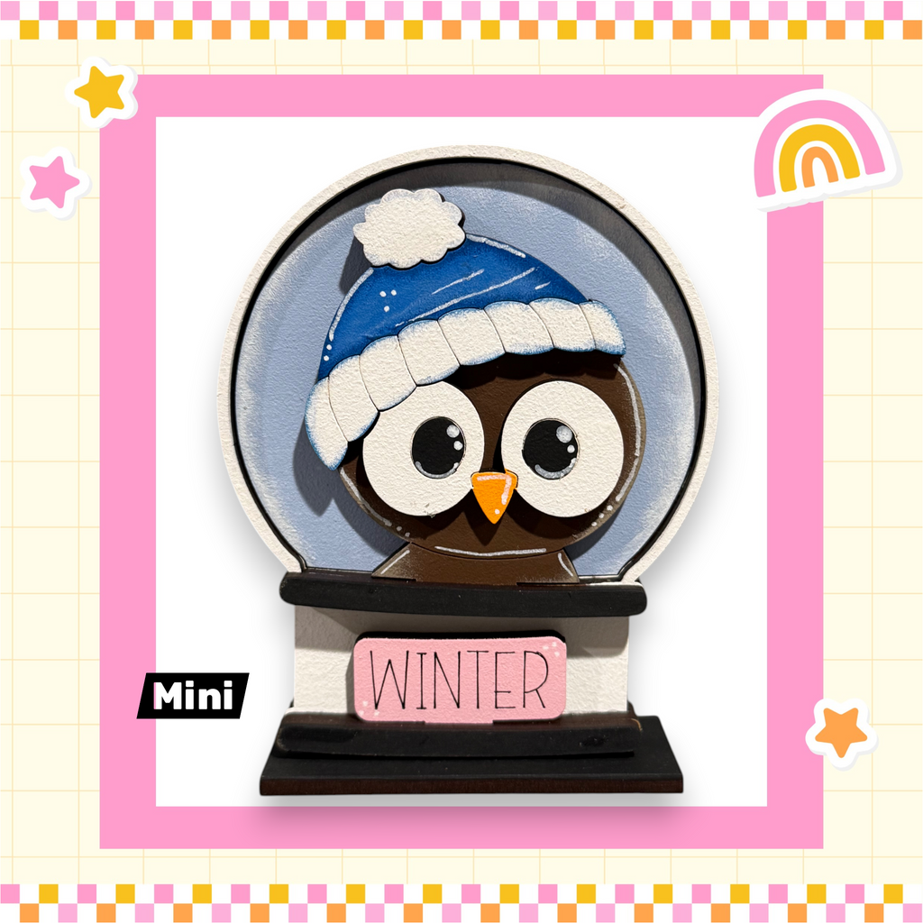 A snow globe with an owl wearing a blue hat and the word "WINTER" written on it, set against a pink and yellow background with stars and a rainbow.
