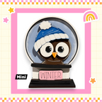 A snow globe with an owl wearing a blue hat and the word "WINTER" written on it, set against a pink and yellow background with stars and a rainbow.