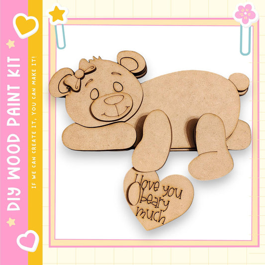 A wooden bear figure with a heart-shaped message attached to it, set against a pink and yellow background.