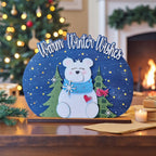 A wooden sign with a polar bear and snowflakes, surrounded by a winter scene, sits on a table with a lit candle and other holiday decorations in the background.