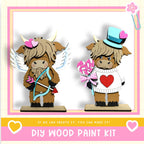 two wooden figurines, one with wings and the other with a heart-shaped hat, both holding candy hearts and bows, set against a pink and white background.
