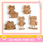 a DIY wood paint kit with five wooden frog figures in various poses, including one sitting on a castle, one holding a book, one holding a stick, one holding a stick and a book, and one holding a stick and a book.