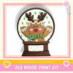 A DIY wood paint kit for creating a wooden snow globe with a gingerbread man figure, set against a pink and white background.