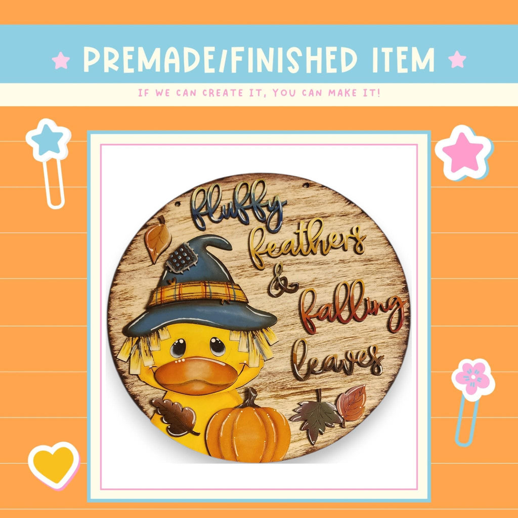 a wooden sign with a duck wearing a witch's hat and holding a pumpkin, surrounded by autumn leaves.